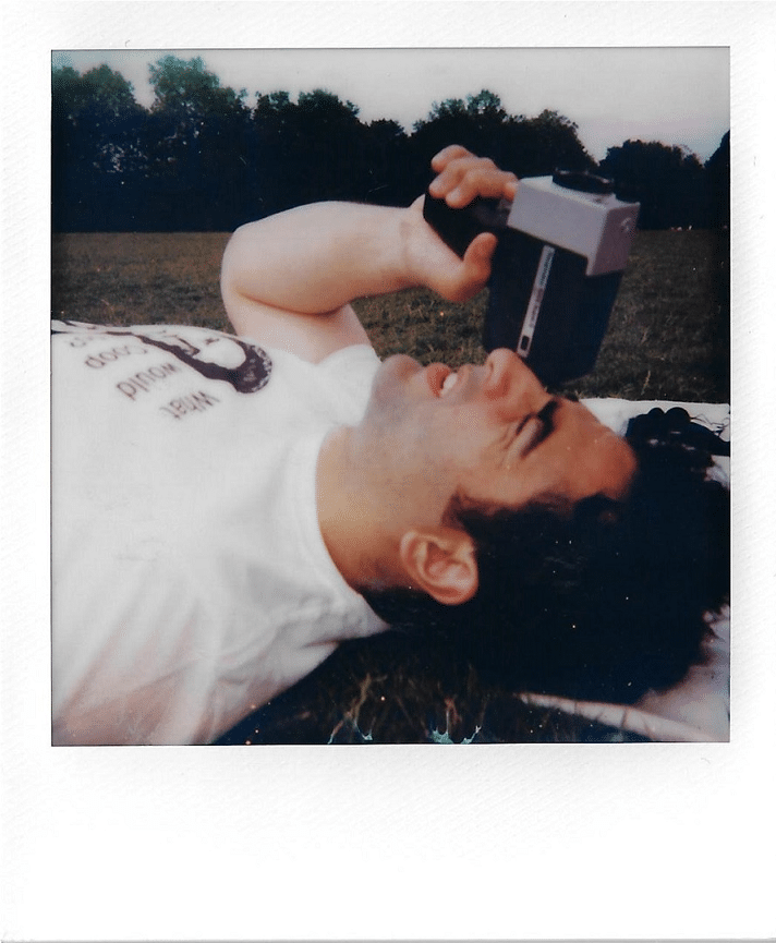 Hero image for Films section. Polaroid picture of Remi Milligan on his back filming the sky with a Super 8 camera.